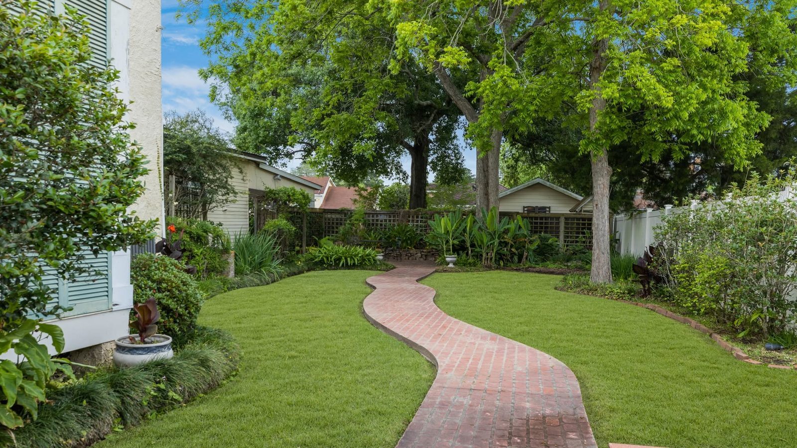 A winding brick path through the manicured gardens of a historic estate, shaded by old trees