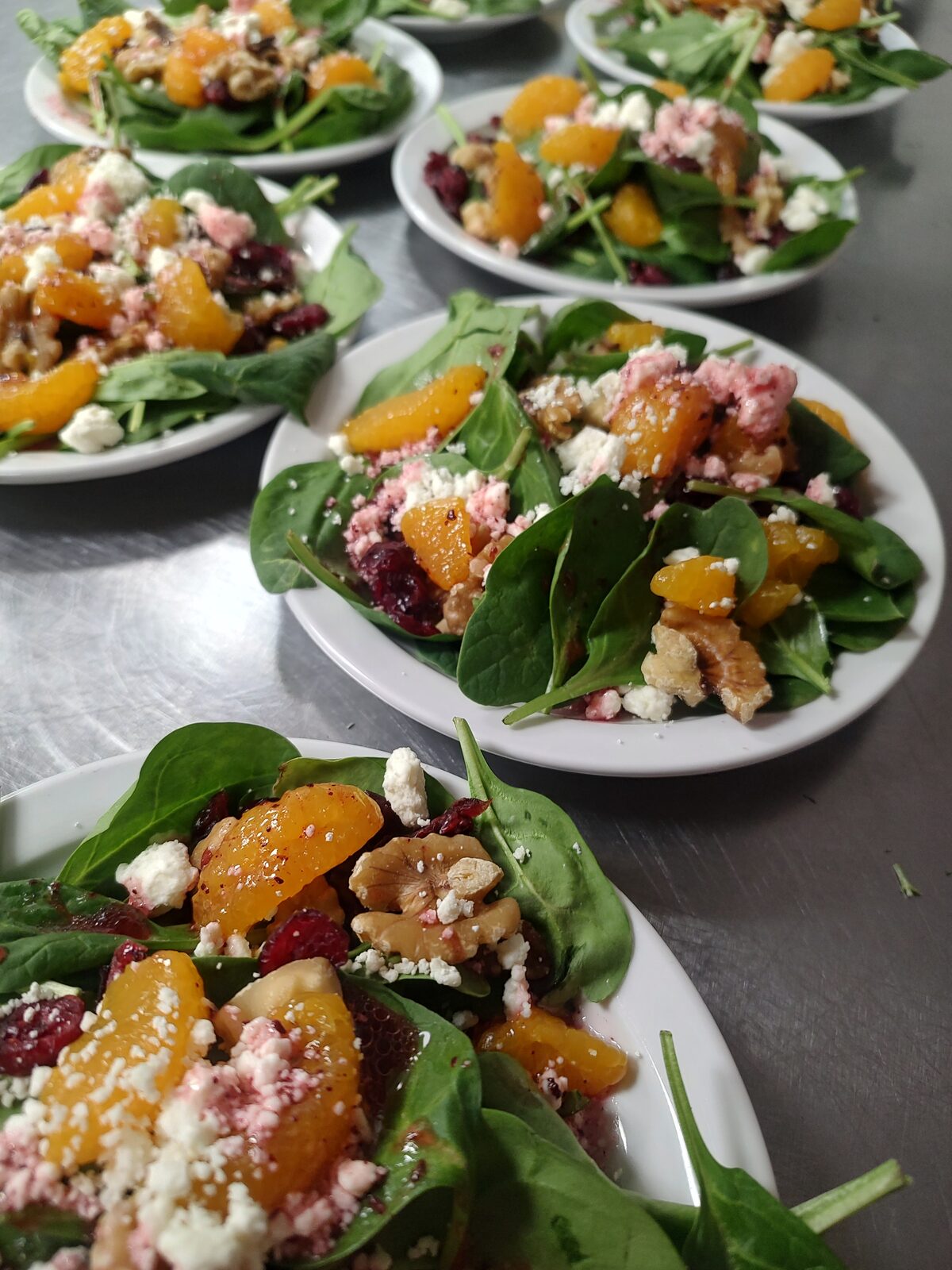 Plated spinach salads with mandarin, candied walnuts, dried cranberries, and goat cheese