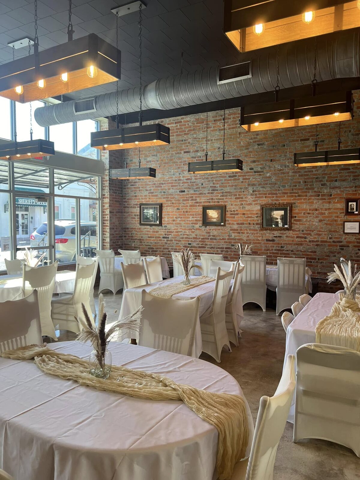 Reception tables dressed in ivory linens and pampas grass centerpieces beneath warm lanterns and exposed brick