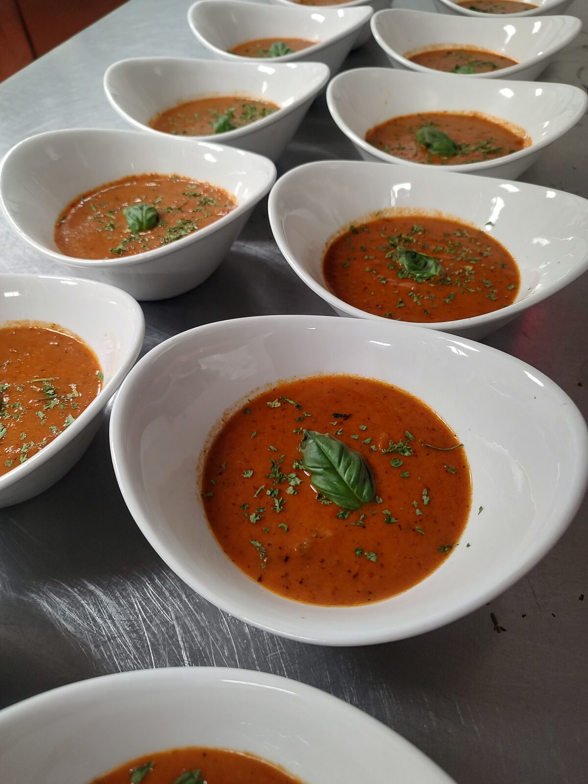 Individual cups of creamy tomato-basil soup, each finished with a fresh basil leaf and a scatter of herbs