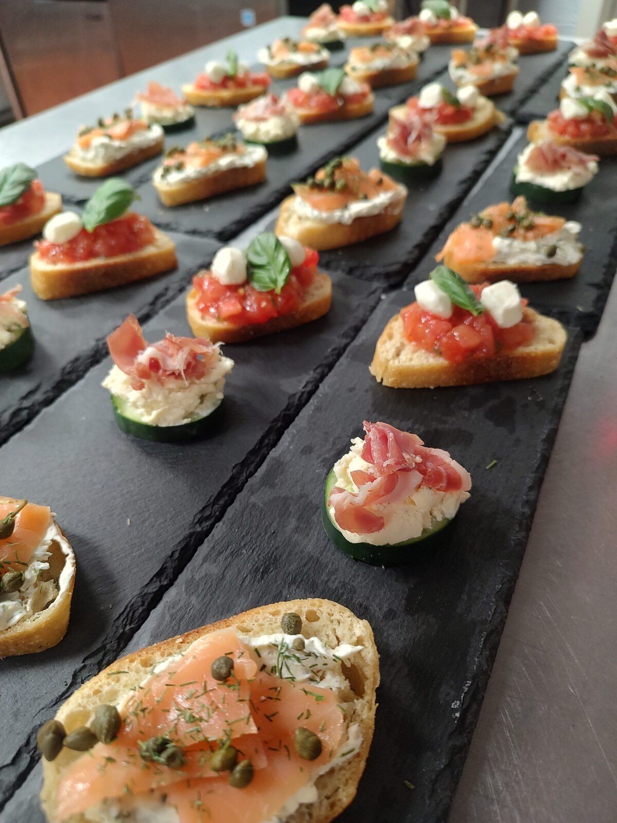 Canapés lined up on a slate board, dressed with fresh herbs and ready to pass