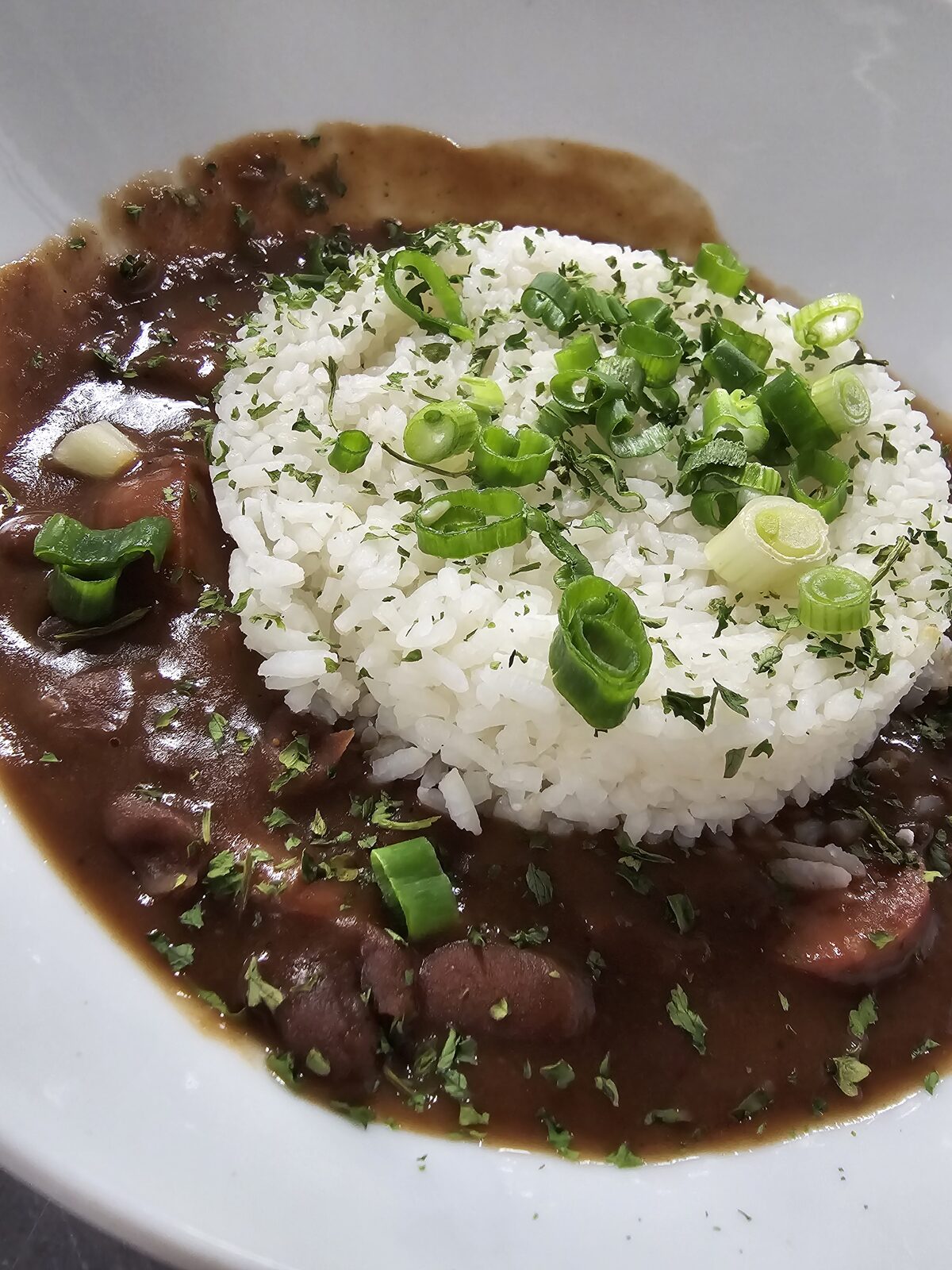 A bowl of slow-simmered red beans and sausage over white rice, topped with sliced green onions