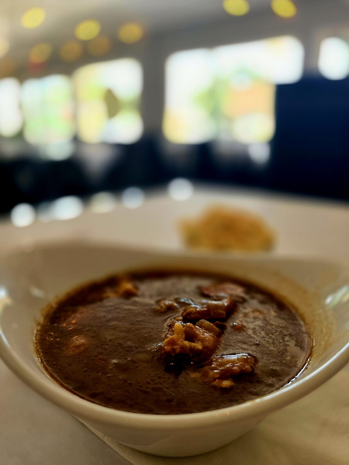 A bowl of dark roux gumbo with tender meat, served tableside in the dining room