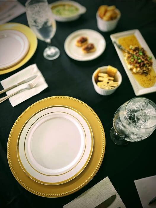 A place setting of gold-rimmed plates on dark linen, surrounded by trays of hors d'oeuvres
